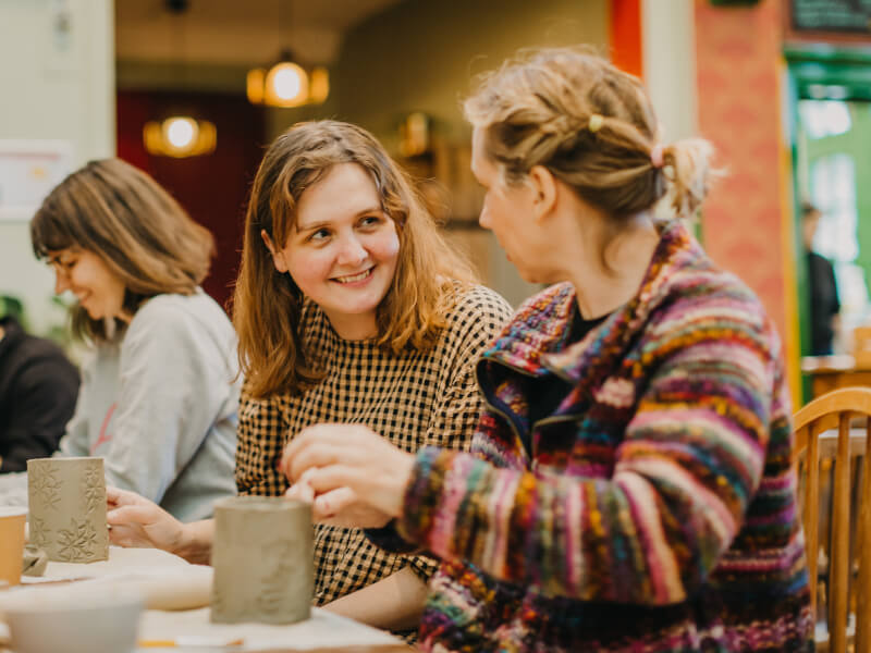 Women smiling at each other as they hand build clay